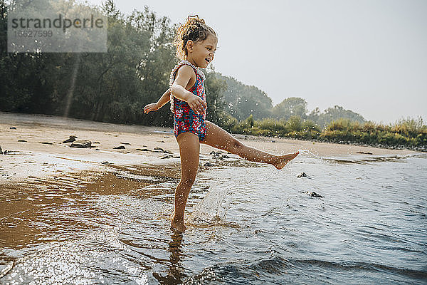 Nettes kleines Mädchen spielt im Wasser am Strand an einem sonnigen Tag