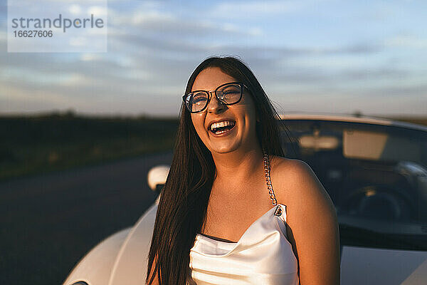 Fröhliche Frau  die lachend vor einem Auto steht