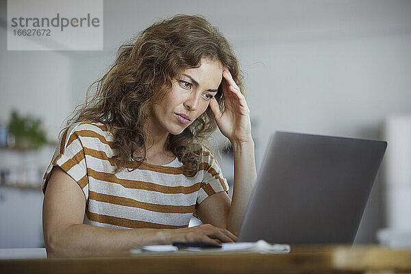 Frau sitzt mit dem Kopf in den Händen und arbeitet zu Hause am Laptop