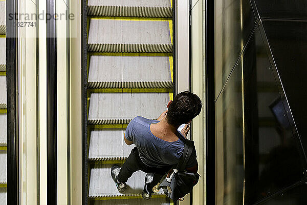 Mann benutzt Smartphone  während er auf einer Rolltreppe in einer beleuchteten U-Bahn steht