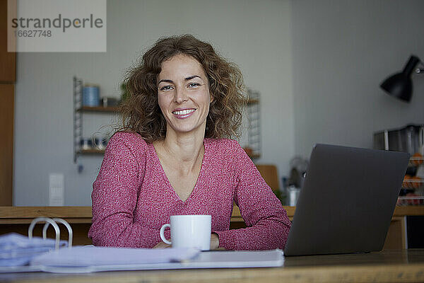Lächelnde Frau  die bei der Arbeit zu Hause einen Laptop benutzt