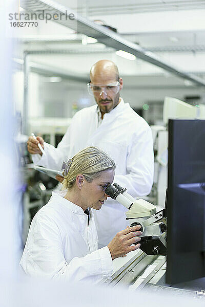 Eine Wissenschaftlerin forscht  während ein männlicher Kollege im Labor in ein Mikroskop schaut