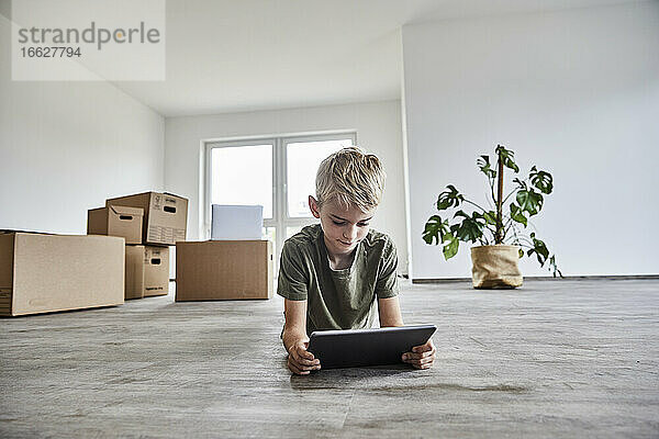 Junge im Liegen beim Spielen auf einem digitalen Tablet in einem neuen Haus