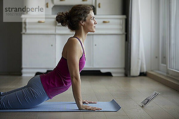 Frau benutzt digitales Tablet während sie zu Hause Yoga macht