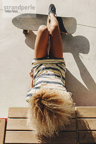 Blonde Afro-Frau mit Skateboard an einem sonnigen Tag liegend