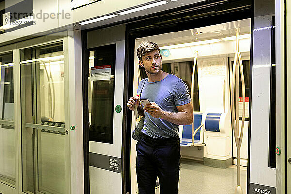 Gut aussehender junger männlicher Pendler  der beim Aussteigen aus einem U-Bahn-Zug am Bahnhof wegschaut