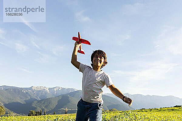 Lächelnder Junge  der ein Flugzeugspielzeug hält  während er vor einem klaren Himmel steht
