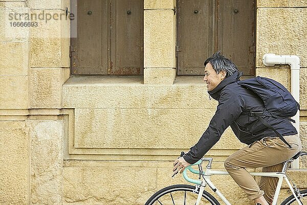 Japanischer Geschäftsmann mittleren Alters  der Fahrrad fährt