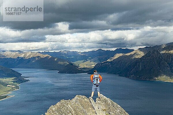 Wanderer steht auf einem Felsen  Ausblick über Lake Hawea  See und Berglandschaft im Abendlicht  Ausblick vom Isthmus Peak  Wanaka  Otago  Südinsel  Neuseeland  Ozeanien