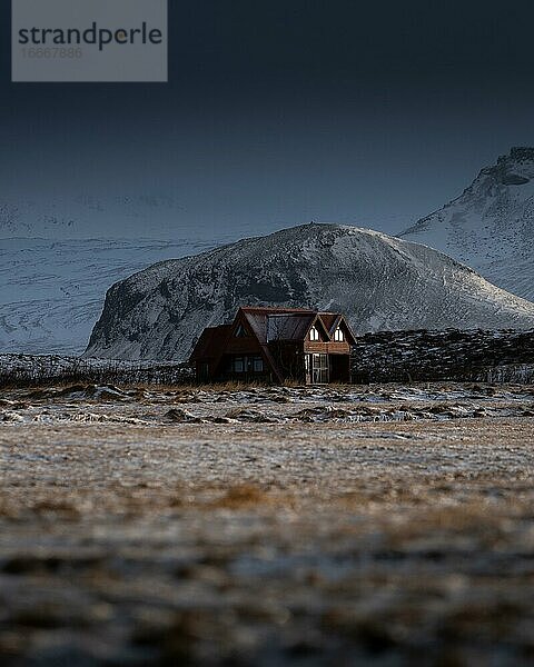 Rotes Haus vor beschneitem Berg mit dramatischer Lichtstimmung  Olafsvik  Island  Europa