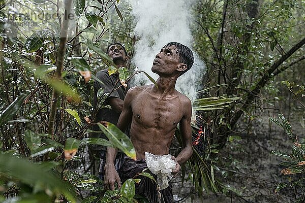 Zwei Honigsammler nach dem Entzünden feuchter Stauden und Blätter mit Brandbeschleuniger um Rauch zu erzeugen  Mongla  Sundarbans  Bangladesch  Asien