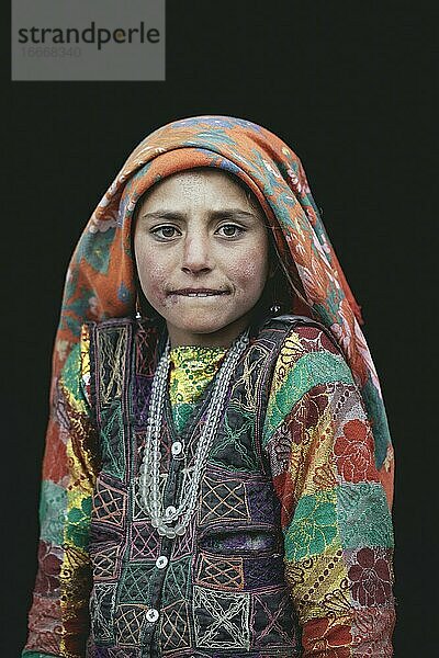 Malia  ein Wakhi-Mädchen mit traditioneller Tracht vor der Tür des Hauses ihrer Familie  Blick in die Kamera  vor schwarzem Hintergrund  Saradh-e-Broghil  Afghanistan  Asien