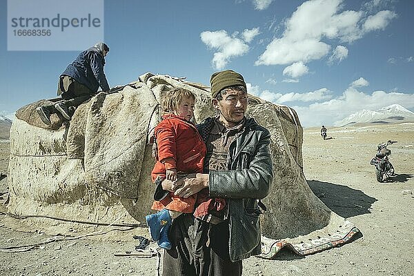 Mann trägt Kind auf dem Arm  nomadische Kirgisen  dahinter traditionelle Jurte  die gerade abgebaut wird  Hochebene von Bozai Gumbaz  Wakhan-Korridor  Badachschan  Afghanistan  Asien