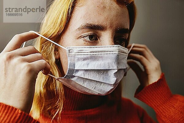 Junge Frau  Teenagerin  hält Einwegmaske zum Schutz vor Corona Viren in der Hand  Studioaufnahme  Köln  Nordrhein-Westfalen  Deutschland  Europa