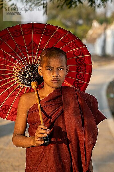 Buddhistischer Mönch steht mit rotem Schirm auf einem Weg  Mingun  Myanmar  Asien