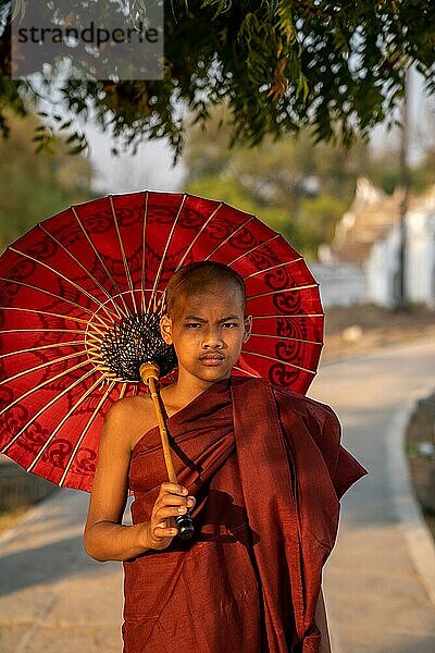 Buddhistischer Mönch steht mit rotem Schirm auf einem Weg  Mingun  Myanmar  Asien