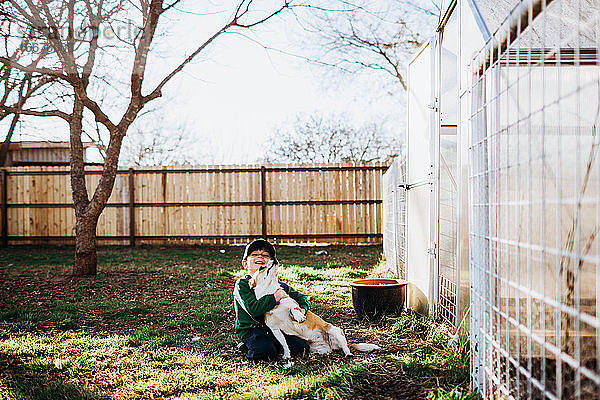 Junger Junge sitzt vor einem Gartenhaus und umarmt einen Corgi-Hund