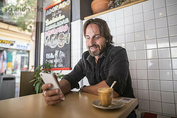 Mann genießt in einem Café  während er auf sein Mobiltelefon schaut
