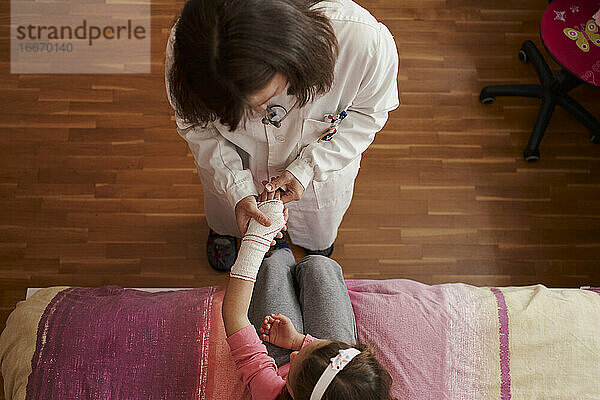 Draufsicht auf eine Ärztin  die den Arm eines kleinen Mädchens verbindet i