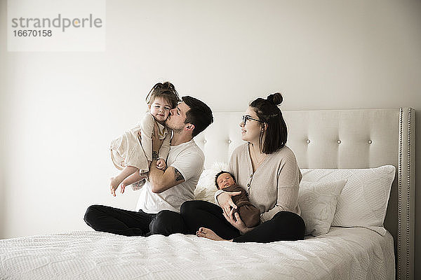 Millennial-Vater küsst seine kleine Tochter  während er mit der Familie zusammensitzt