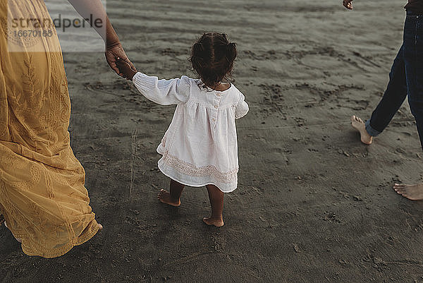 Junges Mädchen und Mutter gehen am Strand und halten sich an den Händen