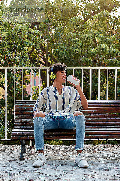 Junger Junge mit Afro-Haar trinkt Kaffee  während er auf einer Bank sitzt