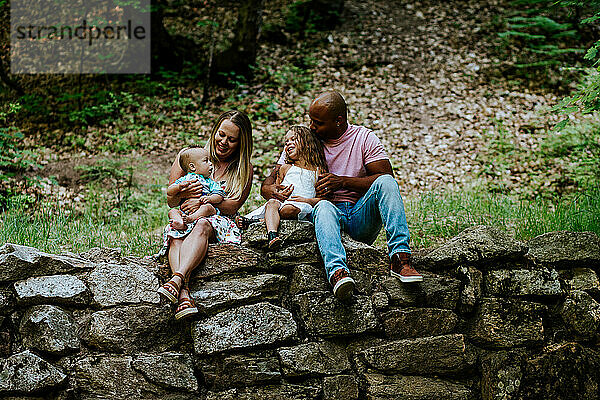 Glückliche junge Familie sitzt auf Felsen im Wald und lächelt