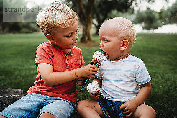 Junges weißes Kleinkind gibt Bruder Eis in einem heißen Sommertag