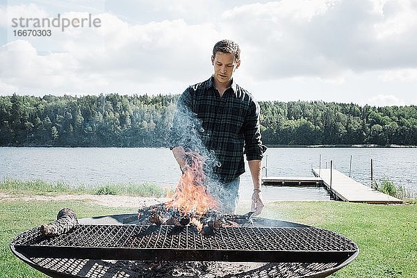 Mann beim Grillen draußen am Strand in Schweden