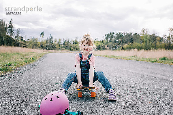 Porträt eines jungen Mädchens  das auf einem Skateboard sitzt und lächelt