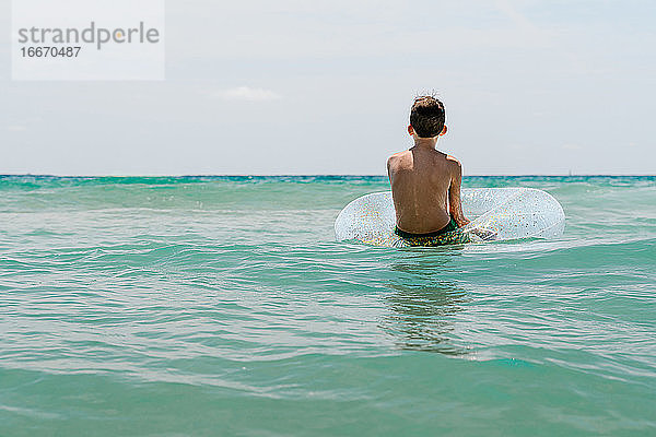 entspannter weißer Junge schwimmt in einem Schwimmer im Meer und genießt die ruhigen Wellen im Sommer. Rückwärts horizontales Foto