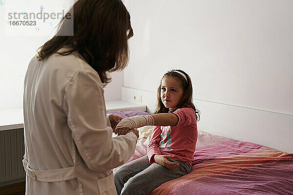 Seitenansicht einer Ärztin  die den Arm eines kleinen Mädchens in ihrem Zimmer verbindet. Hausarzt Konzept
