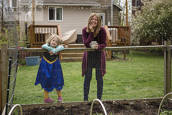 Eine Mutter und ein kleines Mädchen im Prinzessinnenkleid stehen am Rande eines Gartens