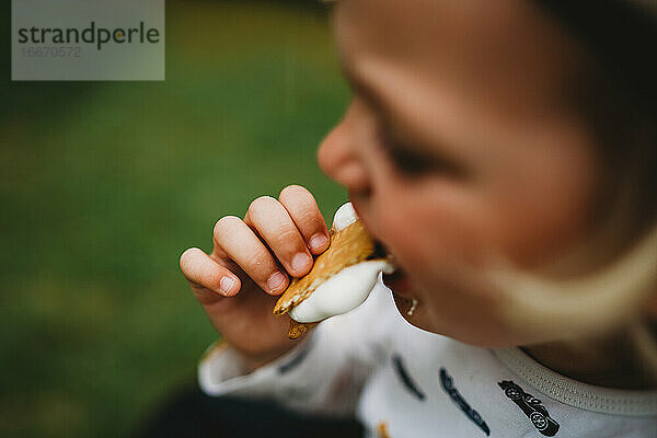 Nahaufnahme von Kinderhand beim Essen von Smores mit geschmolzenem Marshmallow