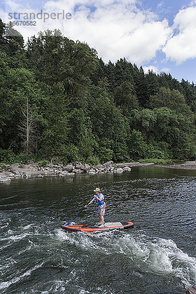 Ein junger Mann genießt den Fluss auf seinem Standup-Paddleboard in Oregon.