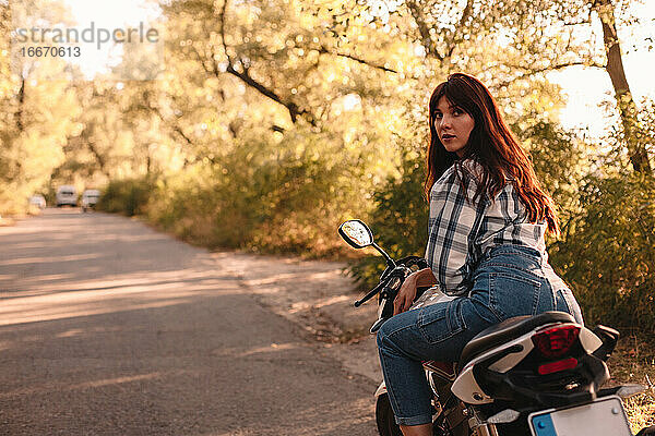 Junge Frau schaut über die Schulter  während sie auf einem Motorrad auf der Straße sitzt