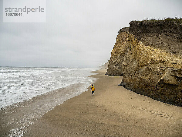 Einsamer junger Mensch  der an einem grauen Tag an einem verlassenen kalifornischen Strand spazieren geht