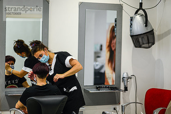 Friseurin bei der Arbeit mit Gesichtsmaske beim Styling eines jungen Mädchens