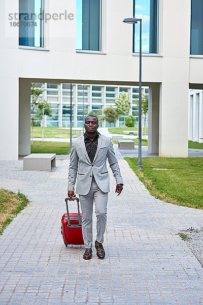 Afroamerikaner in einem weißen Anzug und einem roten Koffer.