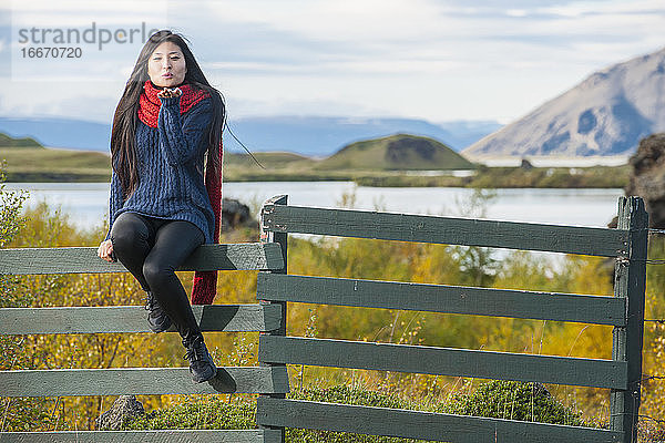schöne Frau  die auf einem Zaun am Myvatn-See sitzt