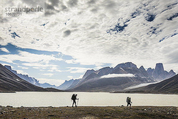 Silhouettierte Rucksacktouristen wandern am Ufer eines Bergsees entlang.