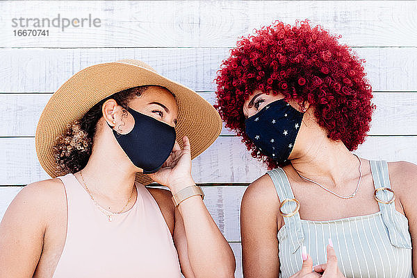 Zwei lateinische Frauen mit Maske in einer sorglosen Haltung auf einem weißen Hintergrund