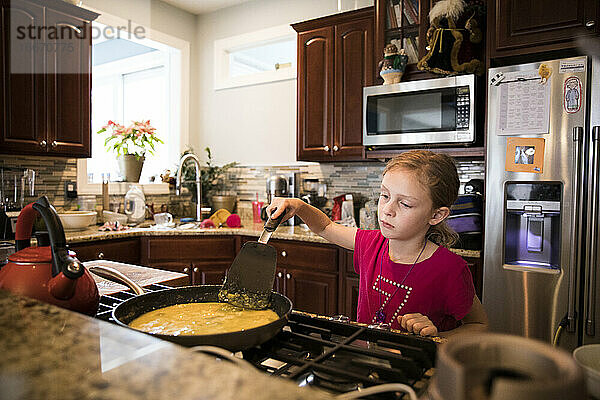 Candid Image of Unsmiling Young Girl Cooking Eggs In Messy Kitchen