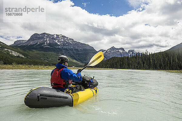 Ein Mann paddelt auf einem gelben Floß durch ein weites Tal im Banff National Park.