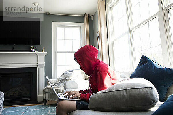 Wide Side View of Tween Boy in Hooded Sweatshirt Arbeiten an Laptop