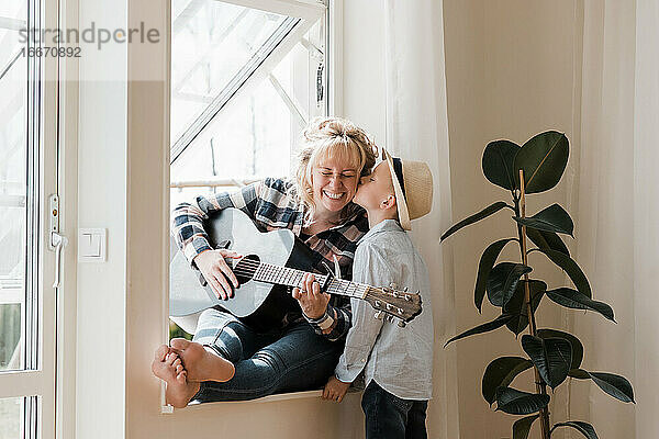 Frau  die zu Hause Gitarre spielt  während ihr Sohn ihr einen Kuss gibt