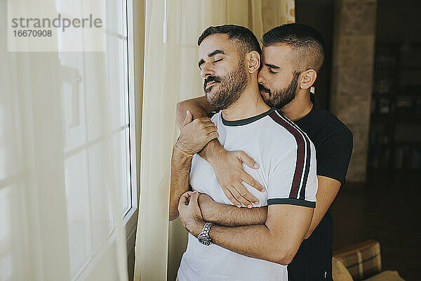 Homosexuelles Paar  das sich zu Hause am Fenster umarmt