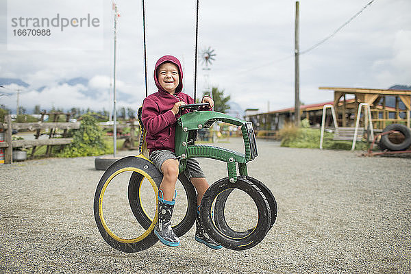 glücklicher Junge sitzt auf einem Traktor aus recycelten Reifen