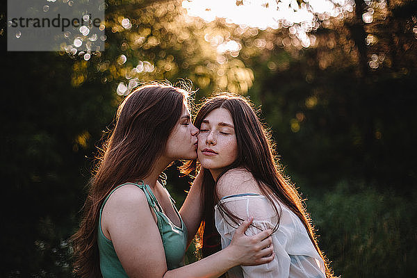 Junge Frau küsst ihre Freundin auf die Wange im Wald im Sommer