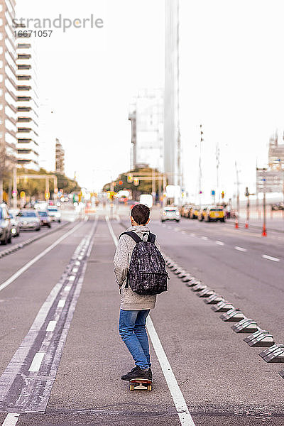 Rückansicht eines jungen Teenagers mit Rucksack auf dem Skateboard in der Stadtstraße